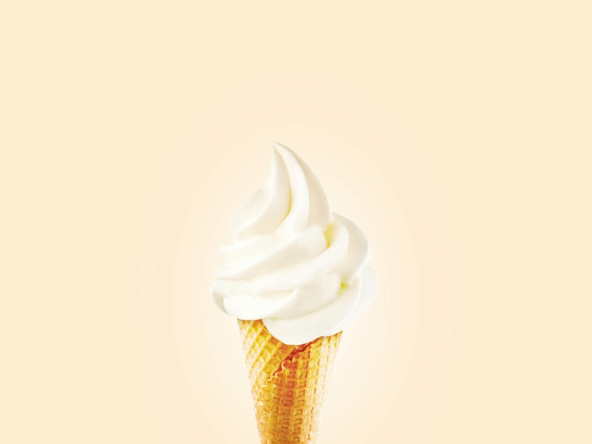 Close-up of a creamy soft serve ice cream cone on a bright background.